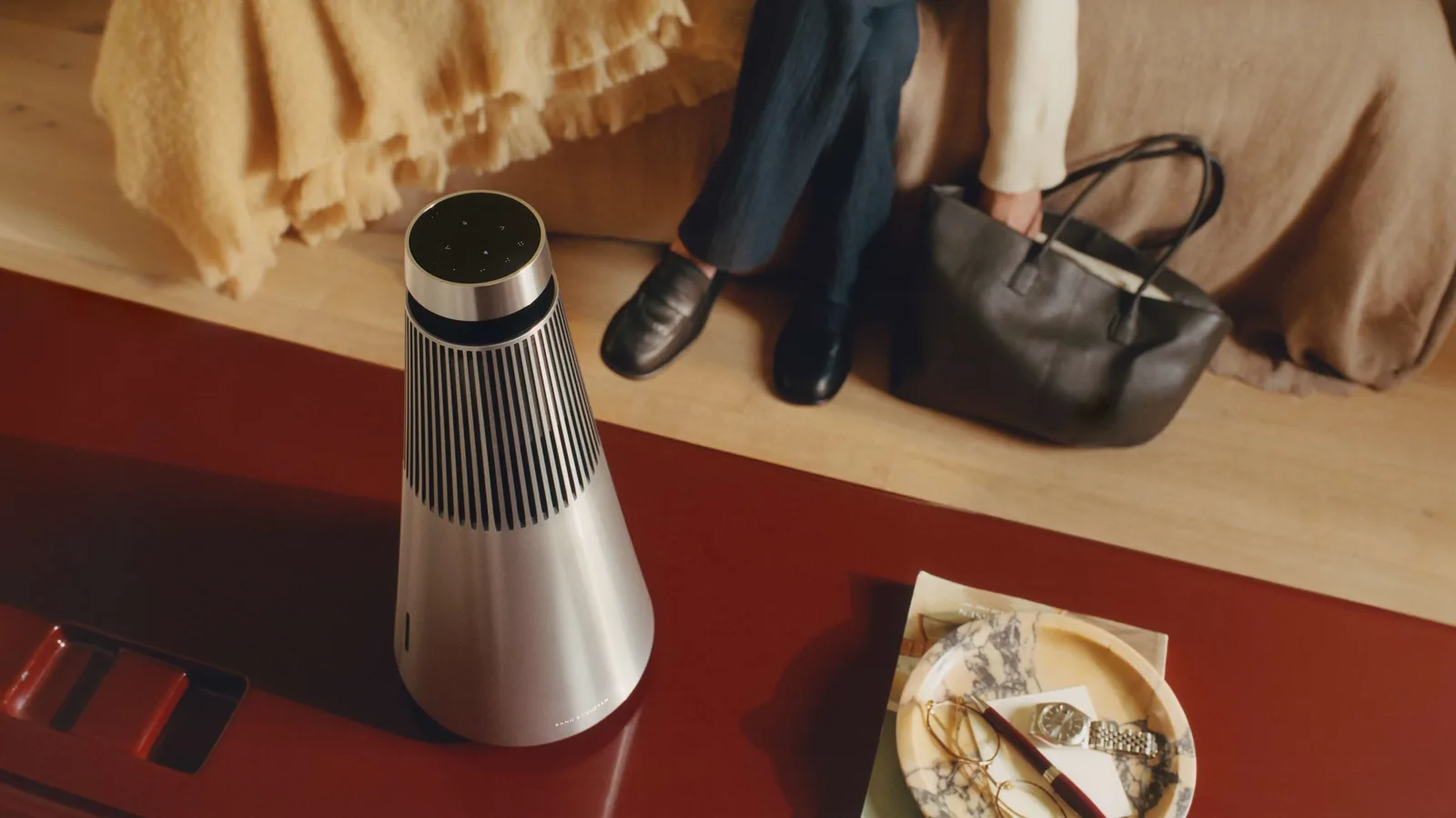 Bang and Olufsen Beosound 2 in aluminum standing on a red floor next to a sofa