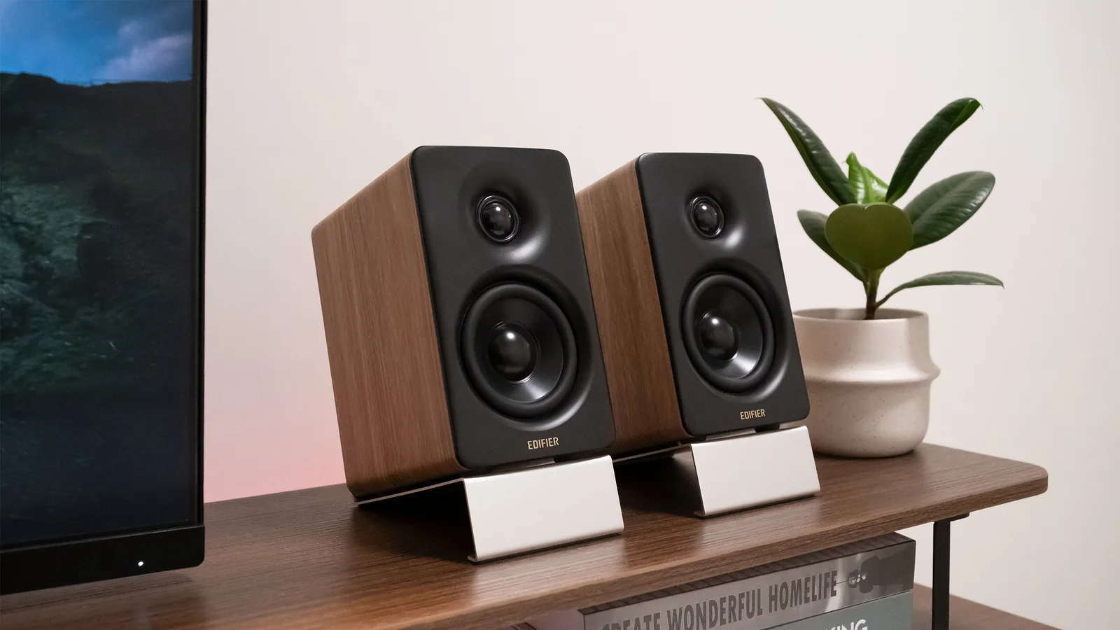Edifier M60 speakers on angled stands on a wooden desk shelf next to a plant