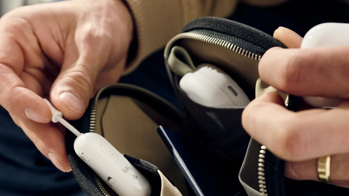 Hands holding a white AirFly Pro 2 transmitter with its pairing buttons visible