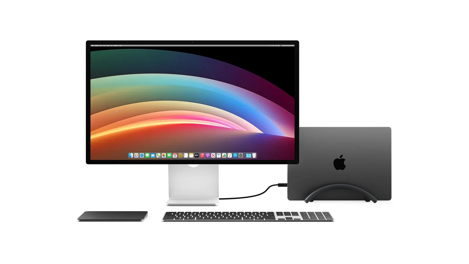 Closed MacBook in a BookArc Flex stand connected by one cable to an external display, with a keyboard and trackpad on the desk